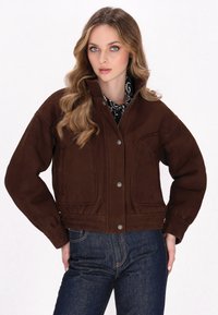 Brun ruskindsjakke med høj krave, frontknapper, sidelommer, med et cropped design og struktureret overflade.