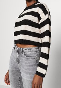 Černobílý pruhovaný krátký pletený svetr s dlouhými rukávy; textura žebrované tkaniny a kulatý výstřih; kombinován s vybledlými šedými džíny.