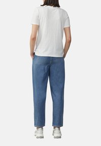 T-shirt blanc à manches courtes, jean bleu taille haute avec une coupe décontractée, et baskets gris clair avec des accents de design et des semelles texturées.