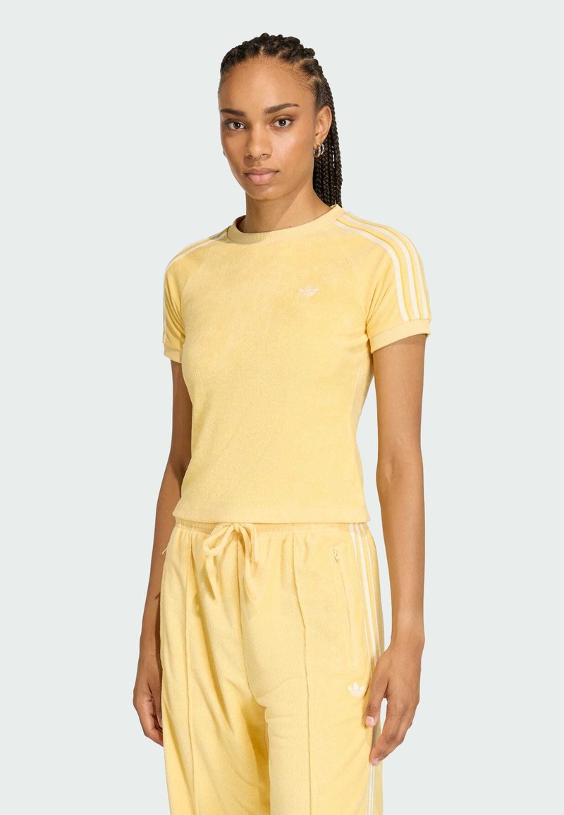 Žltý atletický top vyrobený z textúrovanej tkaniny, s krátkymi rukávmi, okrúhlym výstrihom a bielymi pruhmi na ramienkach.