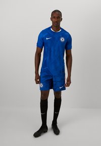 Blauwe voetbaloutfit met geometrische patronen, witte accenten en het clublogo. Inclusief korte mouwen, shorts en kniehoge zwarte sokken.