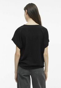 Juoda trumpomis rankovėmis viršūnė su laisvu siluetu, tekstūruota medžiaga ir plačiu iškirpimu, derinama su pilkomis aukšto liemens džinsais.