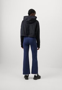 Crna skraćena hoodie s kapuljačom, uparena s mornarsko plavim širokim hlačama. Outfit se odlikuje glatkim materijalom i ležernim dizajnom. Crne tenisice upotpunjuju izgled.