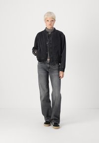 Svart denimjacka med en kortad design, elastisk midja och tryckknappar. Matchad med grå utsvängda jeans och svarta skor.