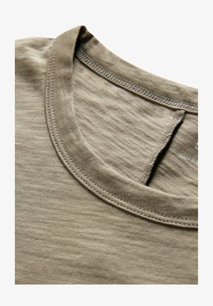 Vaaleanruskea puuvillapaita, jossa on pyöreä kaula-aukko, hieno rakenne ja kontrastiväriset ompeleet kauluksessa ja olkasaumoissa.