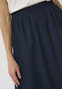 Jupe plissée navy avec une taille élastique, fabriquée en tissu léger. Présente une texture verticale et une silhouette fluide.