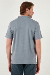 Camisa polo de manga corta en azul pálido con tejido texturizado y un cuello. Presenta aberturas laterales y una pequeña etiqueta con el logo cerca del dobladillo.