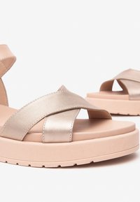 Metallic gold sandals with crossed straps and a cushioned, light beige platform sole. Features a textured upper and pronounced tread.