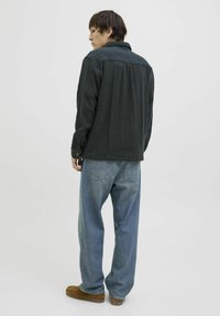 Zwarte, geprofileerde overhemden met lange mouwen, gecombineerd met losse blauwe jeans en bruine instappers, gezien vanuit de achterkant.