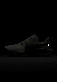 Chaussure de sport de couleur claire avec logo swoosh noir, boucles de lacet multicolores et semelle coussinée, présentée de profil sur fond sombre.