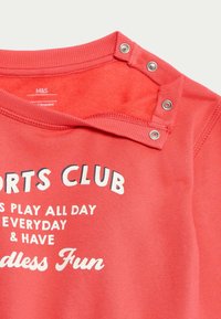 Korala bluza z okrągłym dekoltem, zatrzaski na ramieniu, białego nadrukowanego napisu "KLAB SPORTOWY" oraz dekoracyjnych fraz. Miękki materiał bawełniany.