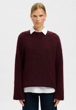 Maglione in borgogna lavorato a maglia con vestibilità ampia, spalle scese e polsini a coste. Indossato sopra una camicia bianca con colletto; texture morbida.