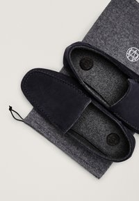 Chaussons en suède bleu marine foncé à enfiler avec doublures en feutre gris et une pochette à cordon assortie en feutre gris, tous deux ornés d'un emblème de logo circulaire.