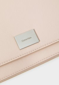 Portafoglio Calvin Klein in morbida pelle testurizzata rosa chiaro con placca in metallo argentato, caratterizzato da cuciture curate e un design semplice e rettangolare.