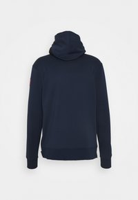 Sweat à capuche bleu marine vu de dos avec manches longues et un petit patch rouge sur le haut du bras.
