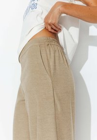 Pantalons beiges à taille élastique avec poches latérales, fabriqués en tissu doux, présentant une texture lisse et de légères plis pour un ajustement décontracté.