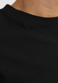 Camiseta de algodón negra con una textura suave y un escote redondo. La tela presenta sutiles variaciones en el tono.