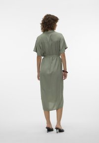 Robe midi vert olive avec des manches courtes, une taille ceinturée et un tissu lisse et fluide. Elle présente un pli au dos pour plus de mouvement.