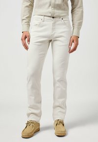 Jeans bianchi in cotone con un design a gamba dritta, dotati di cinque tasche e dettagli di cucitura discreti. Abbinati a scarpe mocassino color beige.