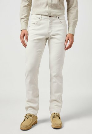 Jeans bianchi in cotone con un design a gamba dritta, dotati di cinque tasche e dettagli di cucitura discreti. Abbinati a scarpe mocassino color beige.