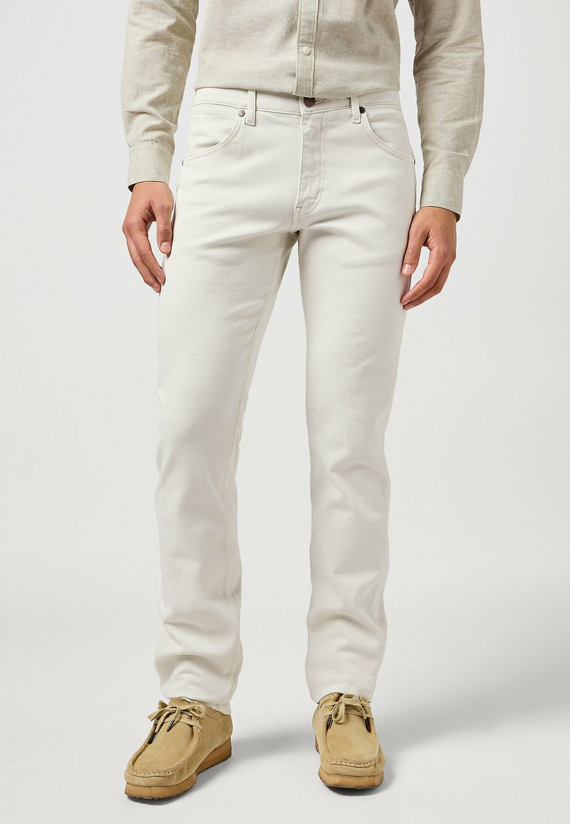 Jeans bianchi in cotone con un design a gamba dritta, dotati di cinque tasche e dettagli di cucitura discreti. Abbinati a scarpe mocassino color beige.