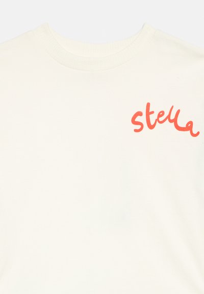 Balta T-krekls ar apaļu kakla izgriezumu un sarkanu kursīvā rakstā uzrakstu "stella" kreisajā krūtīs.
