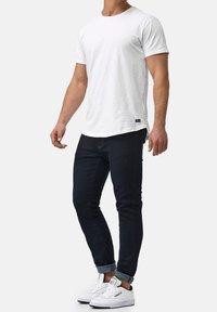 Biała koszulka z okrągłym dekoltem, ciemnoniebieskie dopasowane jeansy oraz białe trampki z niebieskimi akcentami. Jeansy podwinięte na końcach, metka na dole koszulki.