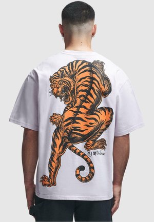 Hvid T-shirt med et stort orange og sort tiger-tryk på ryggen. Korte ærmer, løstsiddende pasform, blødt bomuldsstof.