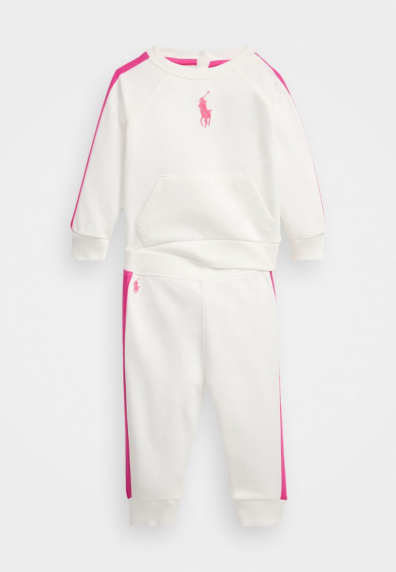 Bela trenirka z roza stranskimi paneli in vezenim logotipom spredaj. Pulover ima sprednji žep in rebraste manšete.