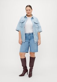Lys blå oversized denimskjorte med korte ermer, kombinert med mid blå denimshorts og skinnende burgunder høyhælte støvler.