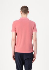 Roze katoenen polo shirt met korte mouwen, minimale kraag en rechte zoom, gecombineerd met marineblauwe broek. Alleen achteraanzicht.