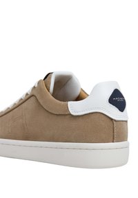 Bruna mockasn sneakers med vita läderdetaljer, vadderad krage och en texturerad gummisula. Har en kontrastfärgad marinblå logotypetikett på hälen.