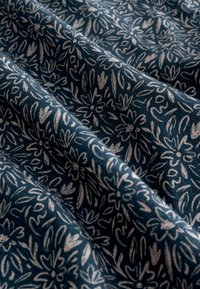 Tamnoplavi materijal s uzorkom cvijeća u svijetloružičastoj boji, s finim linijama i mekom teksturom, prebačen da pokaže dubinu i nabore.