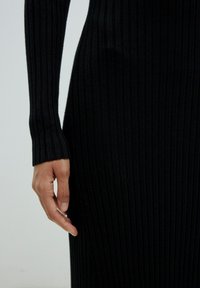 Schwarzes, geripptes Kleid mit langen Ärmeln und enganliegenden Bündchen, das eine schlanke Silhouette schafft. Der Stoff ist weich und dehnbar, was das figurbetonte Design unterstreicht.