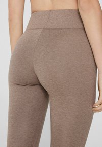 Leggings marrones de cintura alta hechos de un tejido texturizado, que presentan un diseño sin costuras y un ajuste ceñido en la cintura y los muslos.
