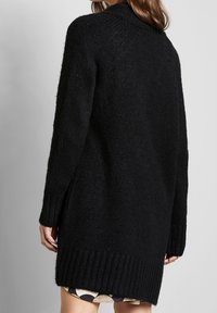 Czarny dzianinowy sweter o teksturowanym wykończeniu, z długimi rękawami i wysokim kołnierzem. Posiada prążkowany dół i boczne rozcięcia dla wygody.