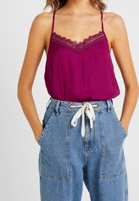 Camisola viola con pizzo, abbinata a pantaloni in denim azzurri a vita alta con grandi tasche e un cordino crema.