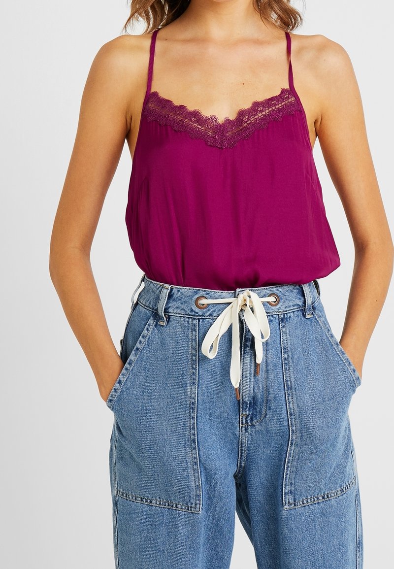 Camisola viola con pizzo, abbinata a pantaloni in denim azzurri a vita alta con grandi tasche e un cordino crema.