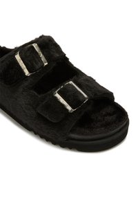 Svart fluffig sandal med öppen tå, två justerbara silverfärgliga spännen och tjock sula, designad för komfort och avslappnad användning.