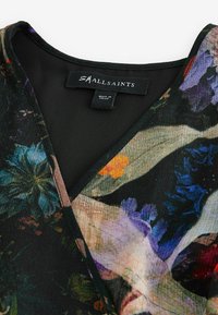 Svart tyg med blommönster i livliga färger. Har en V-ringning och en etikett som läser "SMALLSAINTS." Texturerad yta.
