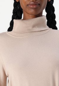 Maglione dolcevita beige chiaro, con texture a coste, design aderente, tessuto morbido, con collo ripiegato e spalle senza cuciture.