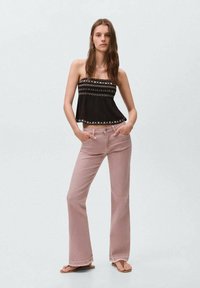 Svart strappless topp med geometrisk brodyr, matchad med ljusrosa utsvängda jeans som framhäver en avslappnad passform och en avslappnad stil.