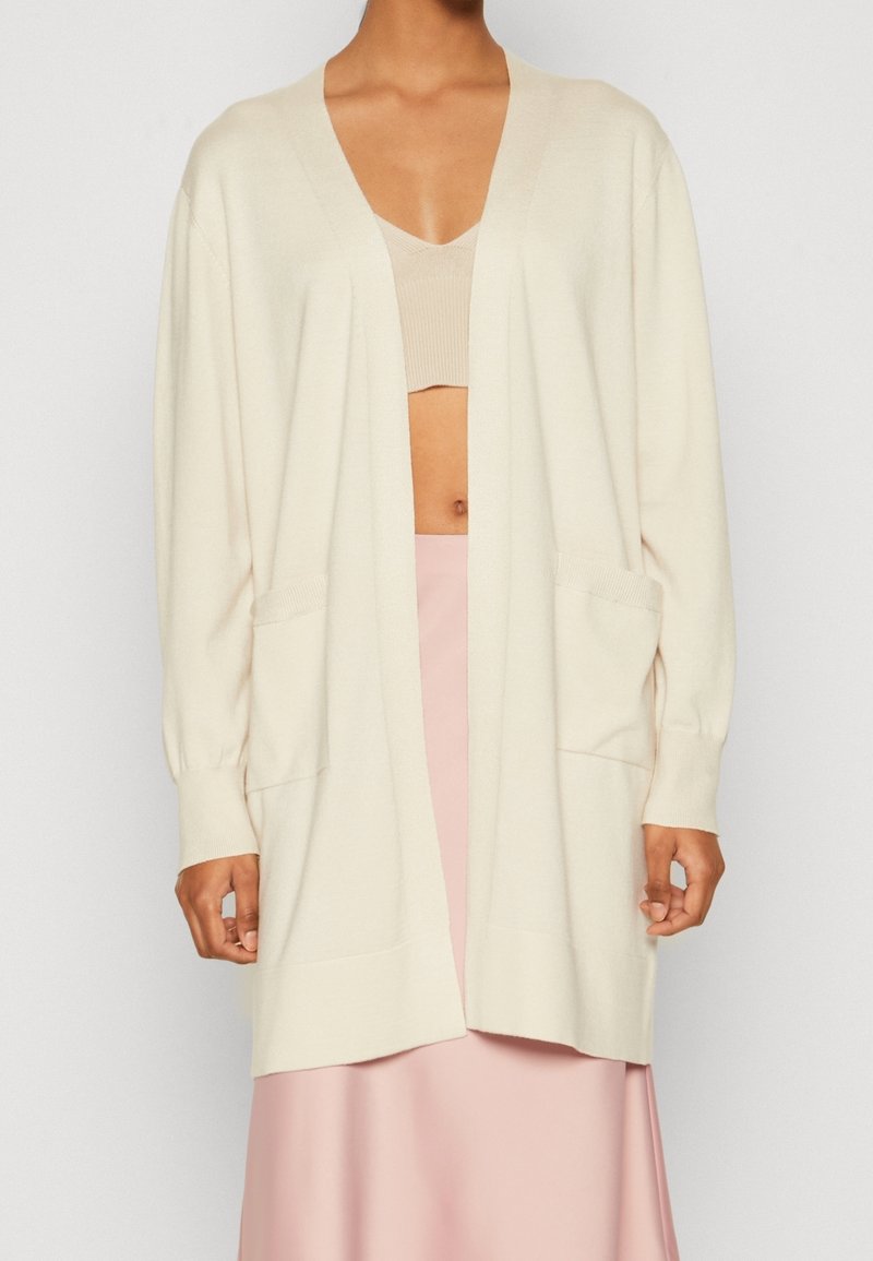 Krämfärgad cardigan i mjukt tyg; har V-ringning, långa ärmar, två framfickor och en avslappnad passform.