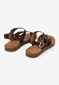 Sandali in pelle marrone con molteplici cinturini regolabili, una soletta imbottita e una suola piatta in gomma con una texture delicata. Accenti in tonalità oro.