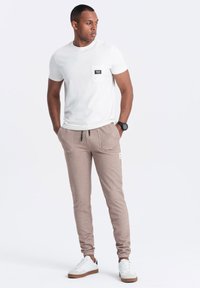 Biała bawełniana koszulka z kieszonką na piersi, w połączeniu z jasnobrązowymi joggerami z dwoma kieszeniami z przodu i czarnymi sznurkami. Białe trampki.