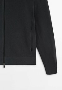 Pull noir en maille avec zip, manches longues et deux poches latérales sur fond blanc.