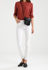 Röd blus med knapprad och två bröstfickor, vita smala jeans och svarta loafers; matchat med en liten svart axelremsväska.