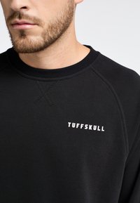 Felpa nera realizzata in materiale morbido. Presenta un colletto tondo, maniche raglan e il logo bianco "TUFFSKULL" nella zona sinistra del petto.