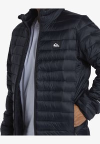 Quiksilver pufferväst i svart nylon med quiltat mönster, hög krage, framdragkedja och sidofickor; har logotyp-patch på bröstet.