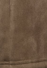 Tissu en suède marron doux avec coutures et détails de surpiqûres visibles, montrant la texture et le matériau en gros plan.